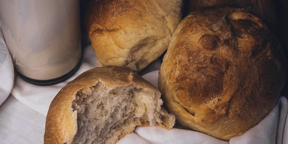 a couple of loaves of bread next to a glass of milk